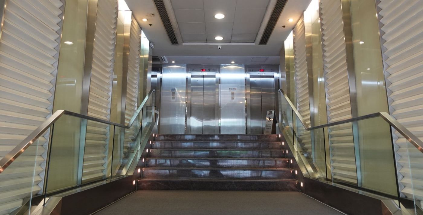 The lobby before the works: a stair with glass balustrades between grey stone walls, with a white ceiling
